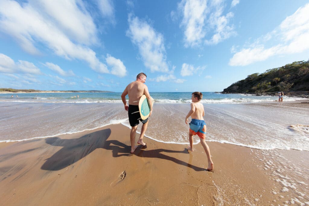 Man and son on Agnes Water Beach going into the surf with a surfboard