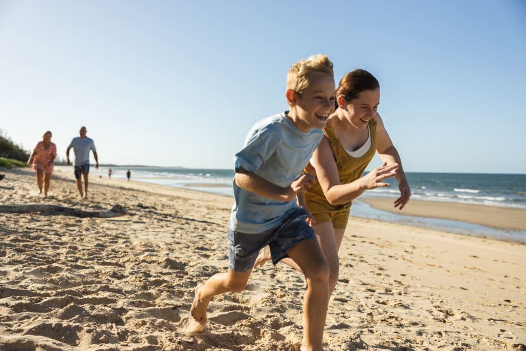 Children running on Woodgate Beach while parents walk behind
