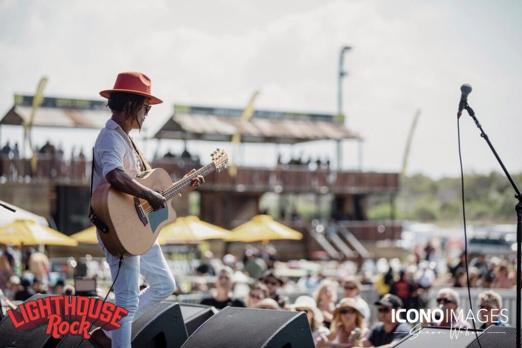 Musician playing a guitar on the stage in front of a crowd at Lighthouse Rocks