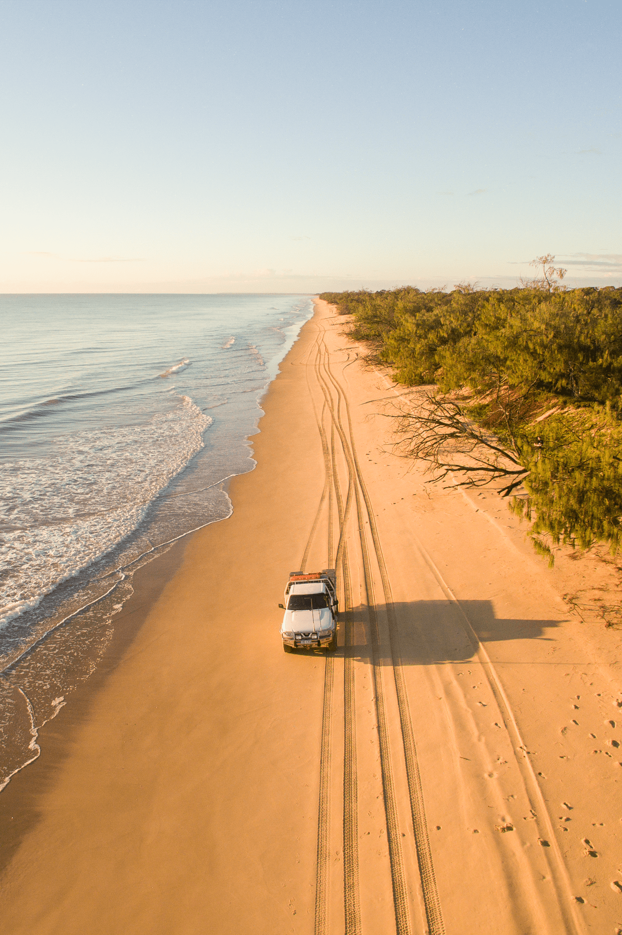 Four‑wheel drive vehicle travelling along the shoreline at Kinkuna Beach in the Bundaberg region, with ocean on one side and coastal bushland on the other.